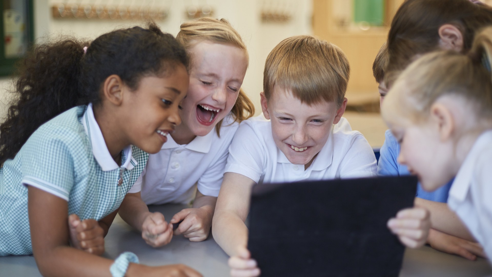 Lachende Schulkinder an einem Pult mit Laptop