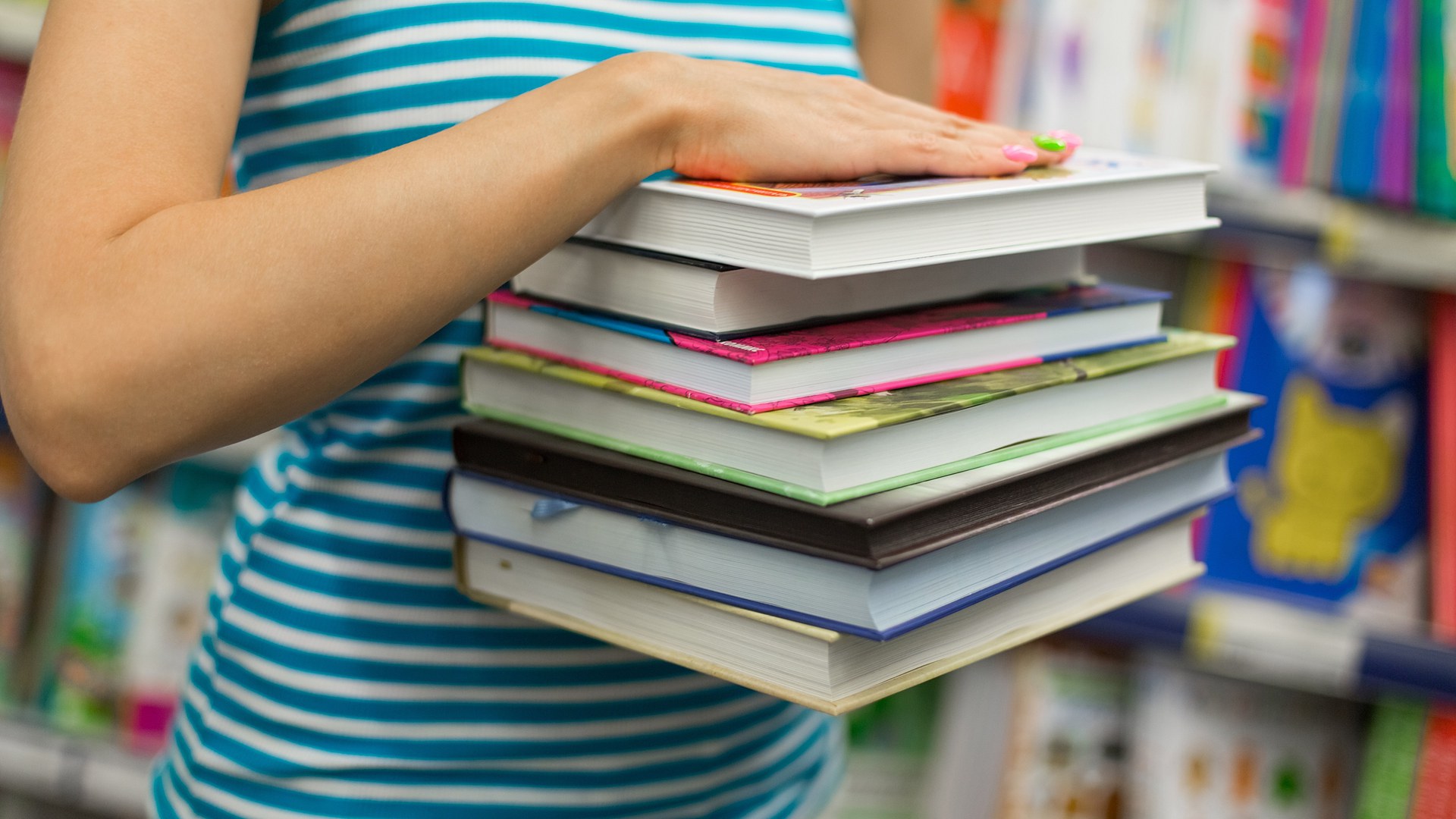 La jeune fille tient une pile de livres scolaires dans ses bras.