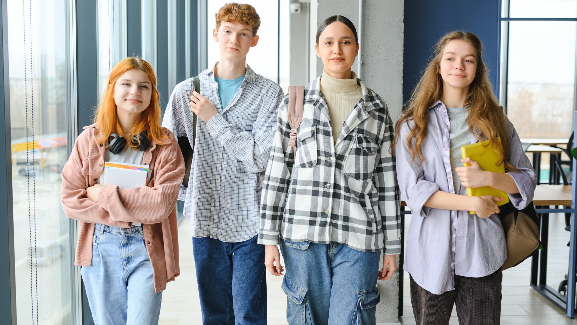 Dans une salle de classe, quatre gymnasiennes et gymnasiens souriants avancent vers l’objectif de l’appareil photo.